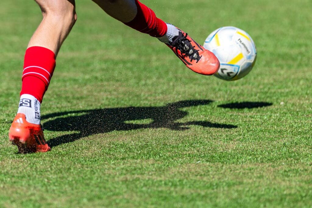 pexels photo 32797683 Soccer player in red kicks a ball mid-air on a sunny day outdoor field.