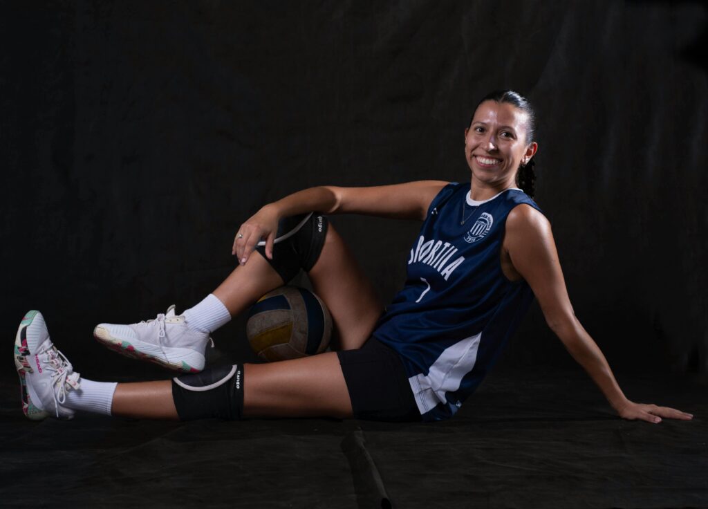 pexels photo 36866638 36866638 Smiling female volleyball player seated with ball, wearing knee pads, jersey, and sneakers.